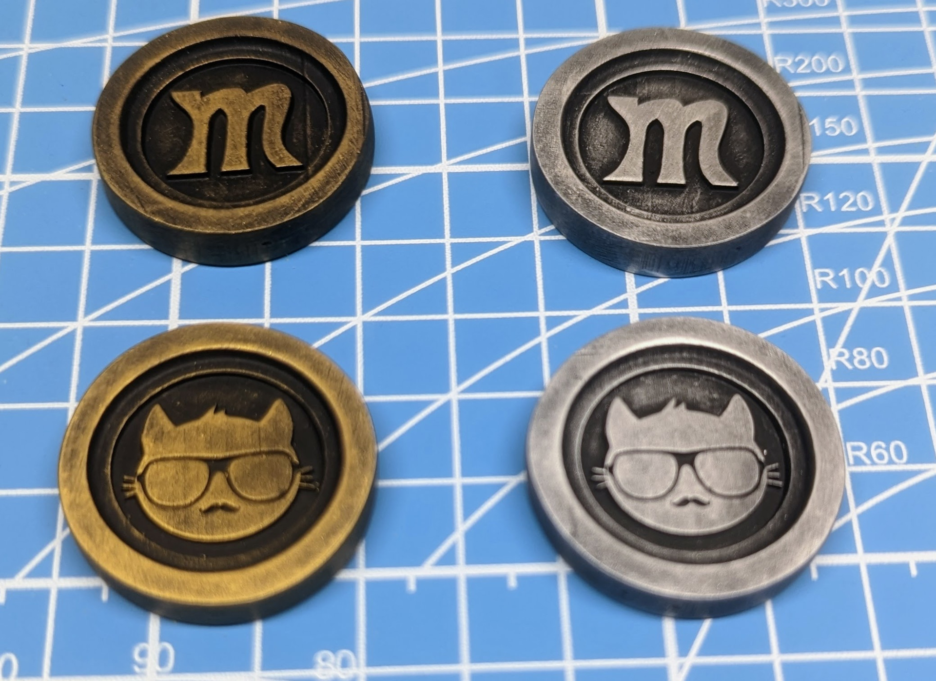 Custom printed resin checkers in silver and gold. One side has the letter M while the other has a cat wearing sunglasses