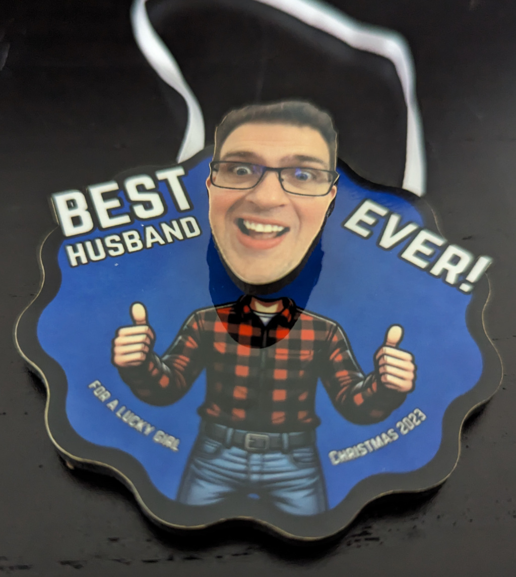 Picture of christmas ornament with scalloped edges. It features a male body wearing jeans and a flannel shirt. The head is stuck out like a bobble head.